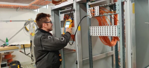 Tecnico esegue test su cablaggio strutturato in armadio di rete Operatore specializzato effettua misurazioni con strumento di rete su pannello di distribuzione con cavi strutturati in rame, all’interno di sala tecnica